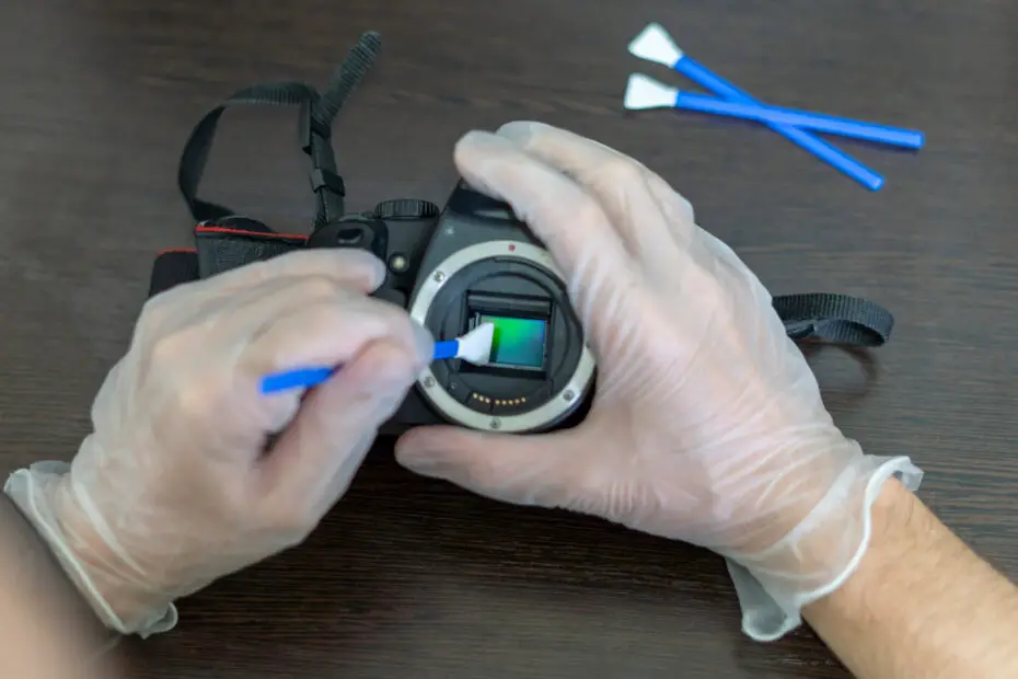 detalhe de mãos de uma pessoa limpando o sensor de uma câmera digital para ilustrar como cuidar do seu equipamento fotográfico