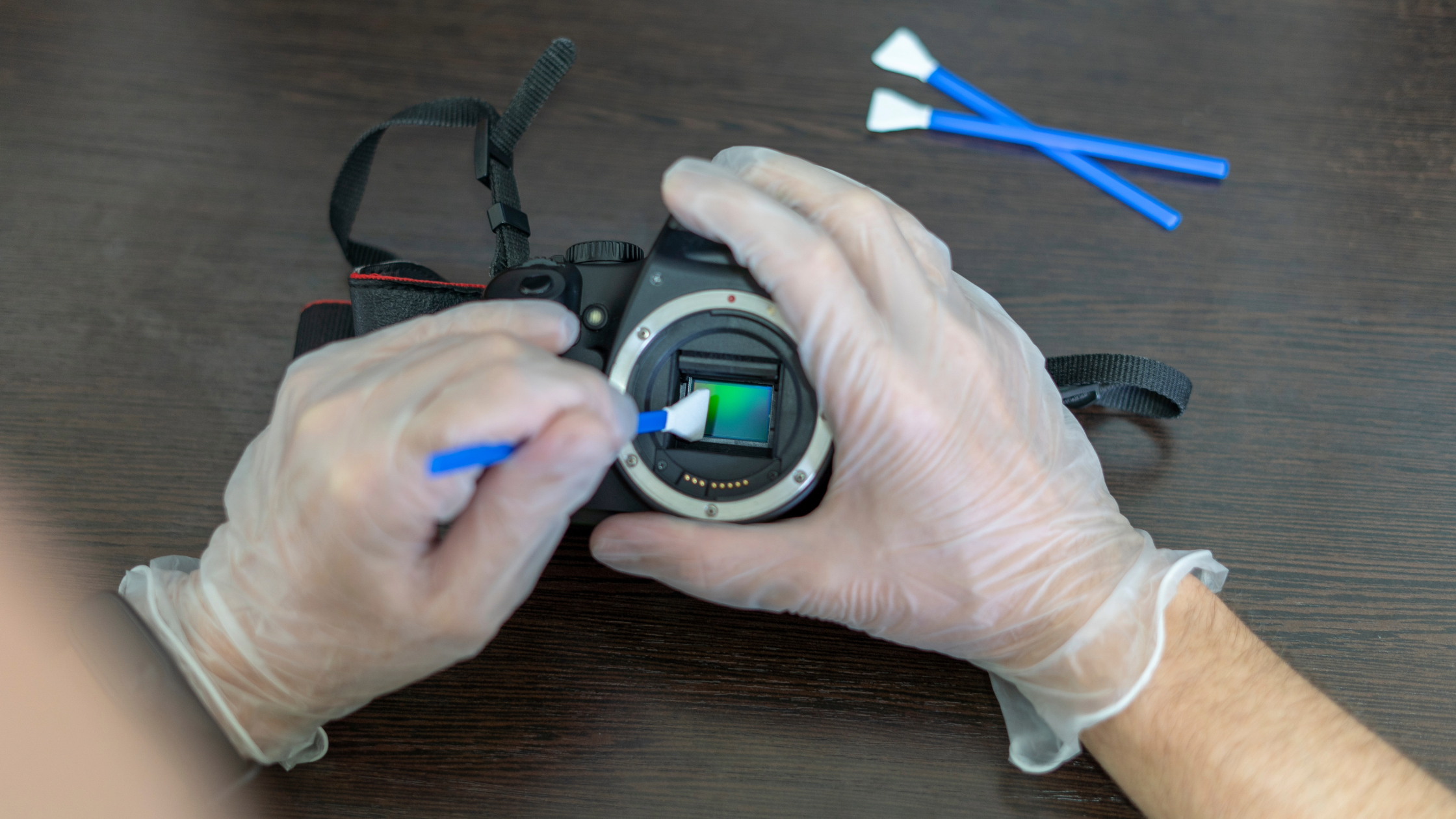 detalhe de mãos de uma pessoa limpando o sensor de uma câmera digital para ilustrar como cuidar do seu equipamento fotográfico